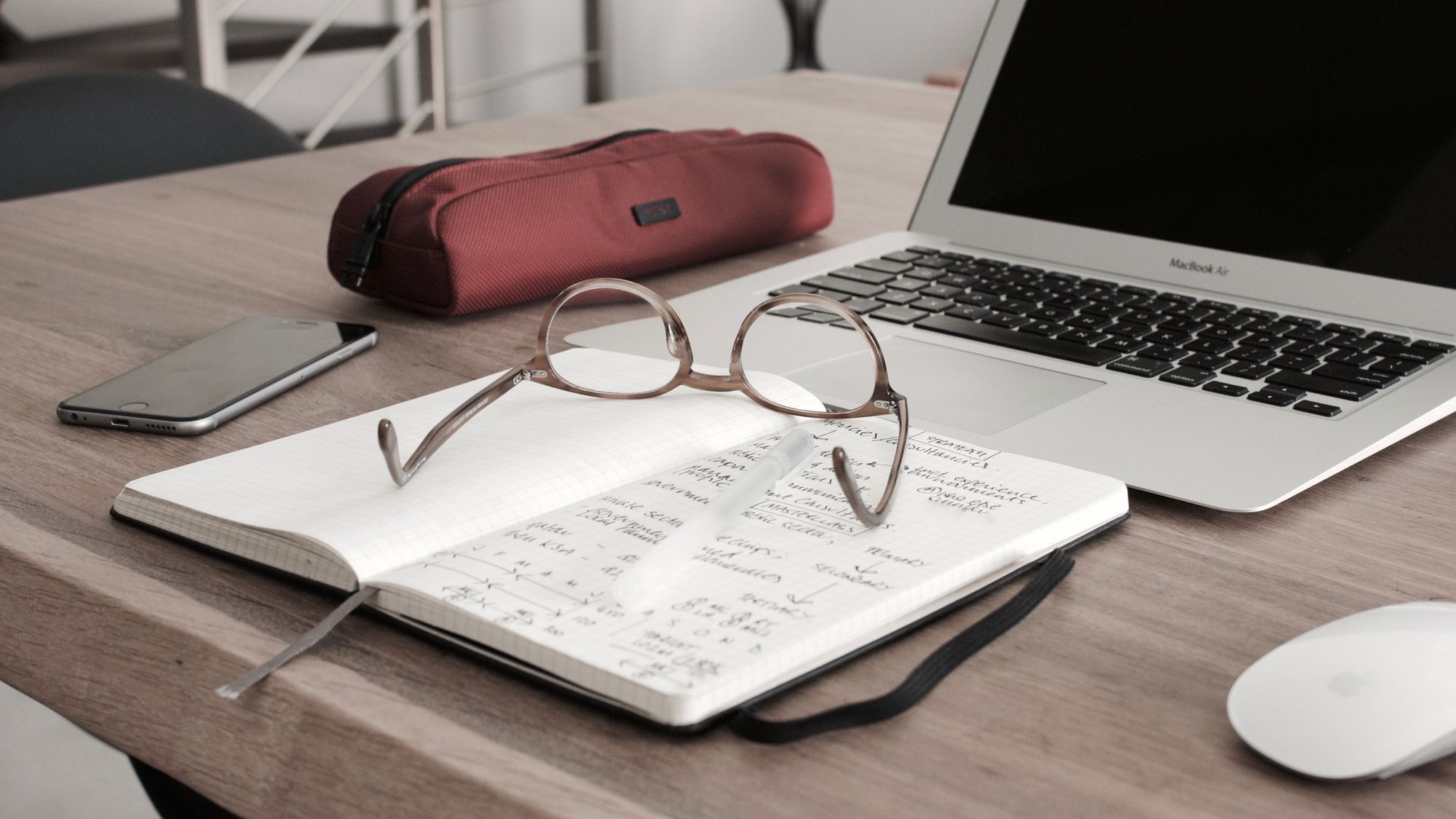 Desk with laptop, notebook and glasses.